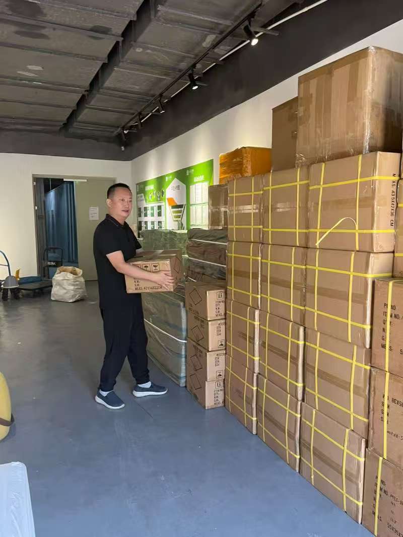Zhiwei Yan moving boxes for a battery electronics sourcing order in a crowded Shenzhen warehouse.