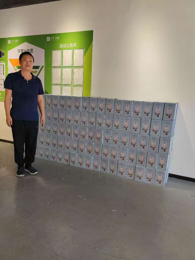 Zhiwei Yan standing with a large consolidated shipment of home appliances in a Shenzhen warehouse